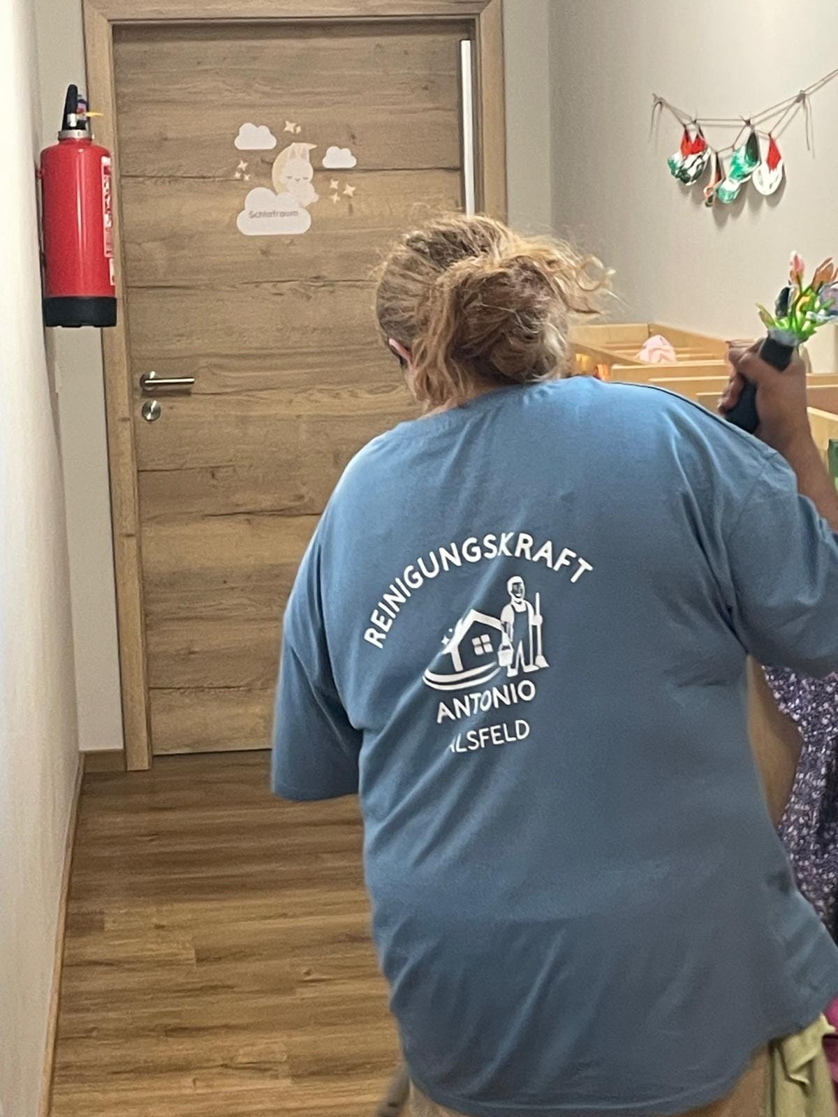 Reinigung im Flur eines Kindergartens, Arbeitskleidung mit Firmenlogo